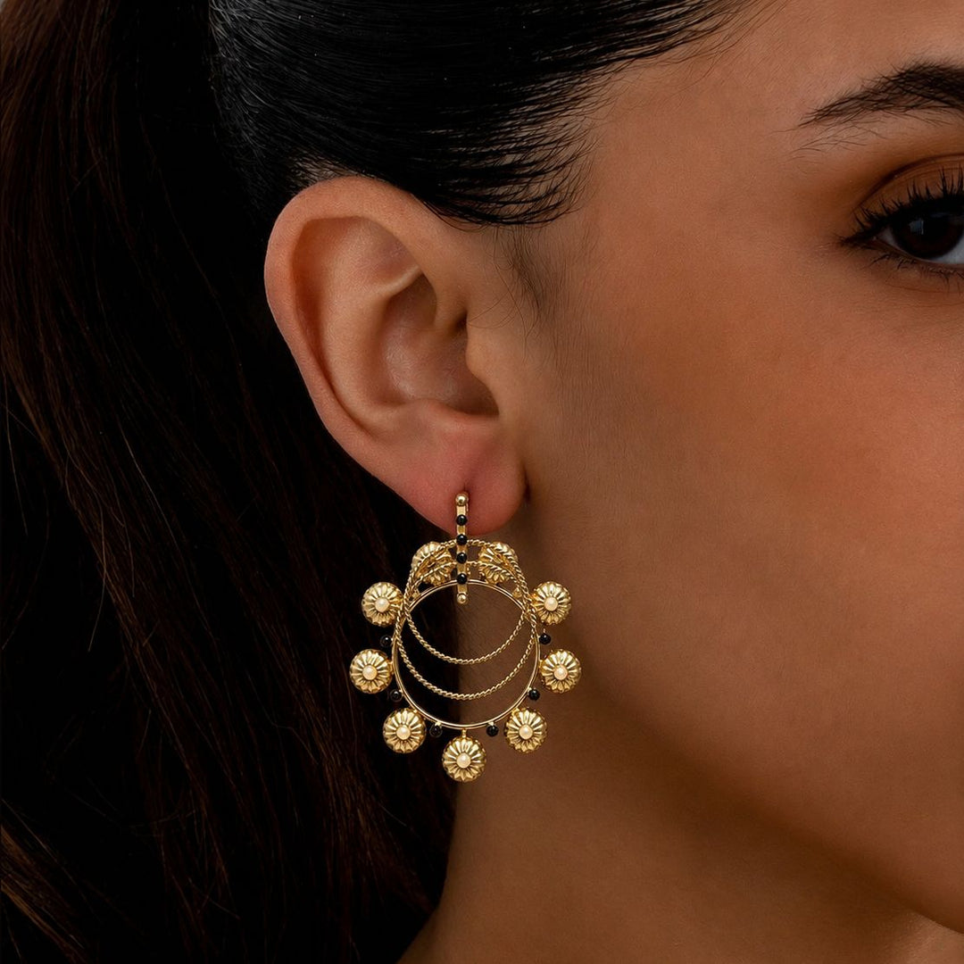 Gold earrings worn by a person with a dark background