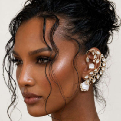 Close-up of a woman wearing an elaborate gold and crystal ear cuff against a neutral background