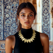 A woman wearing a black top and a golden plume necklace with a matte finish, standing in a beautifully decorated room.