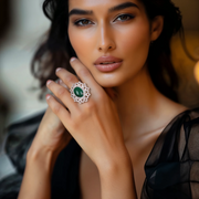 A woman showcasing a silver ring with a green oval center stone and floral halo design.