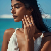 A person wearing a silver and aqua blue ring on their finger, with a blurred background.