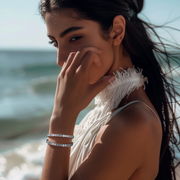 A person wearing a silver bracelet with emerald-cut cubic zirconia stones, standing by the sea.